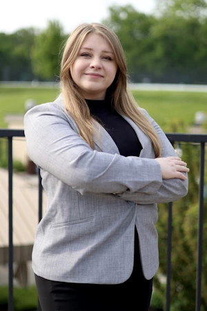 A woman in a suit and blazer stands confidently on a balcony, overlooking the surroundings