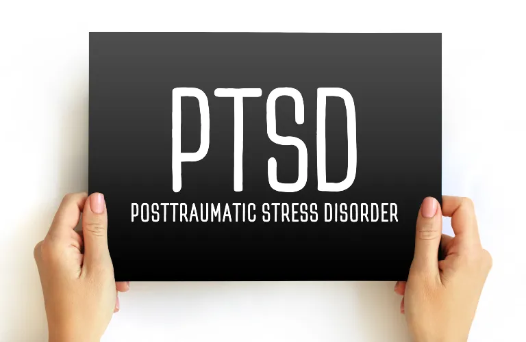 Hands holding a black card with white text reading "PTSD Posttraumatic Stress Disorder" on a white background.