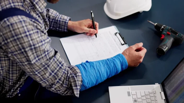 Person with a blue arm cast filling out a clipboard form on a dark desk.