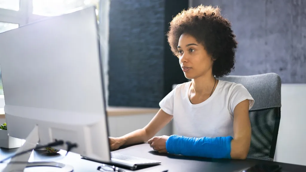 Professional woman with a blue arm cast working at a computer in an office.