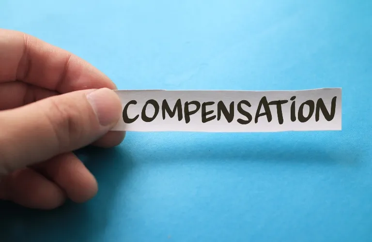 Hand holding a white paper strip with the word "COMPENSATION" in bold black letters on a blue background.